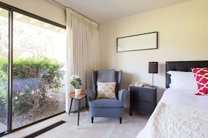 Una habitación de hotel con un ventanal grande, una silla, una mesita de noche y una cama.