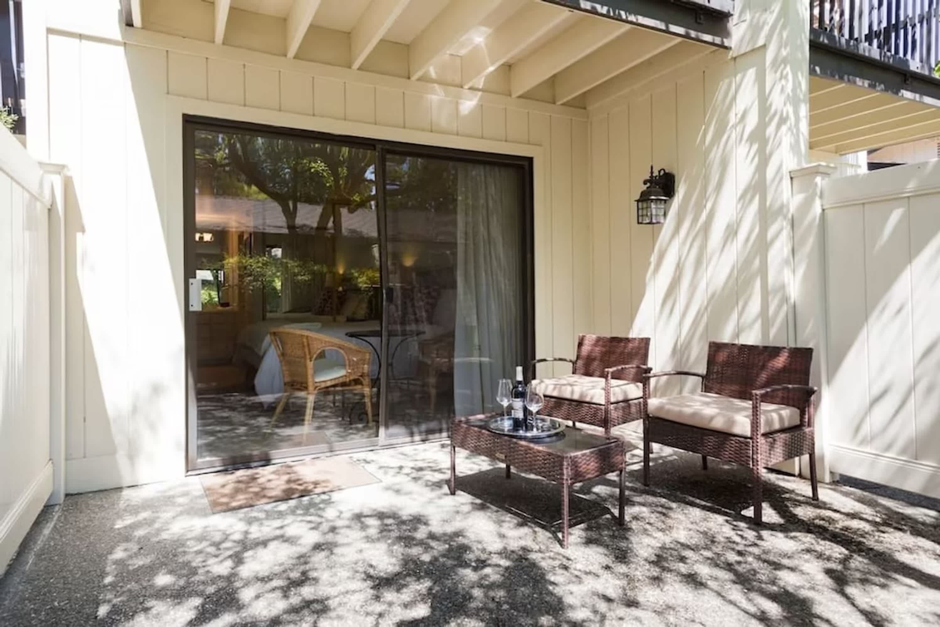 An outdoor patio with wicker furniture, a glass door leading to a room, and a white fence.