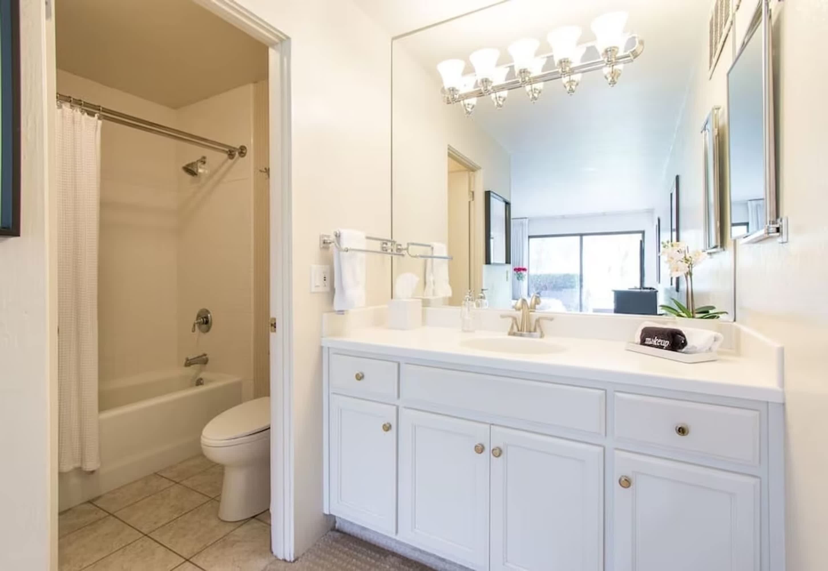 A bathroom with a bathtub, toilet, and vanity with a mirror and lights.