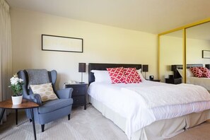 A hotel room with a bed, a chair, a nightstand, a lamp, a mirror, and a framed picture on the wall. - 2BR Napa Getaway Side-by-side Condos Golf View (Napa)