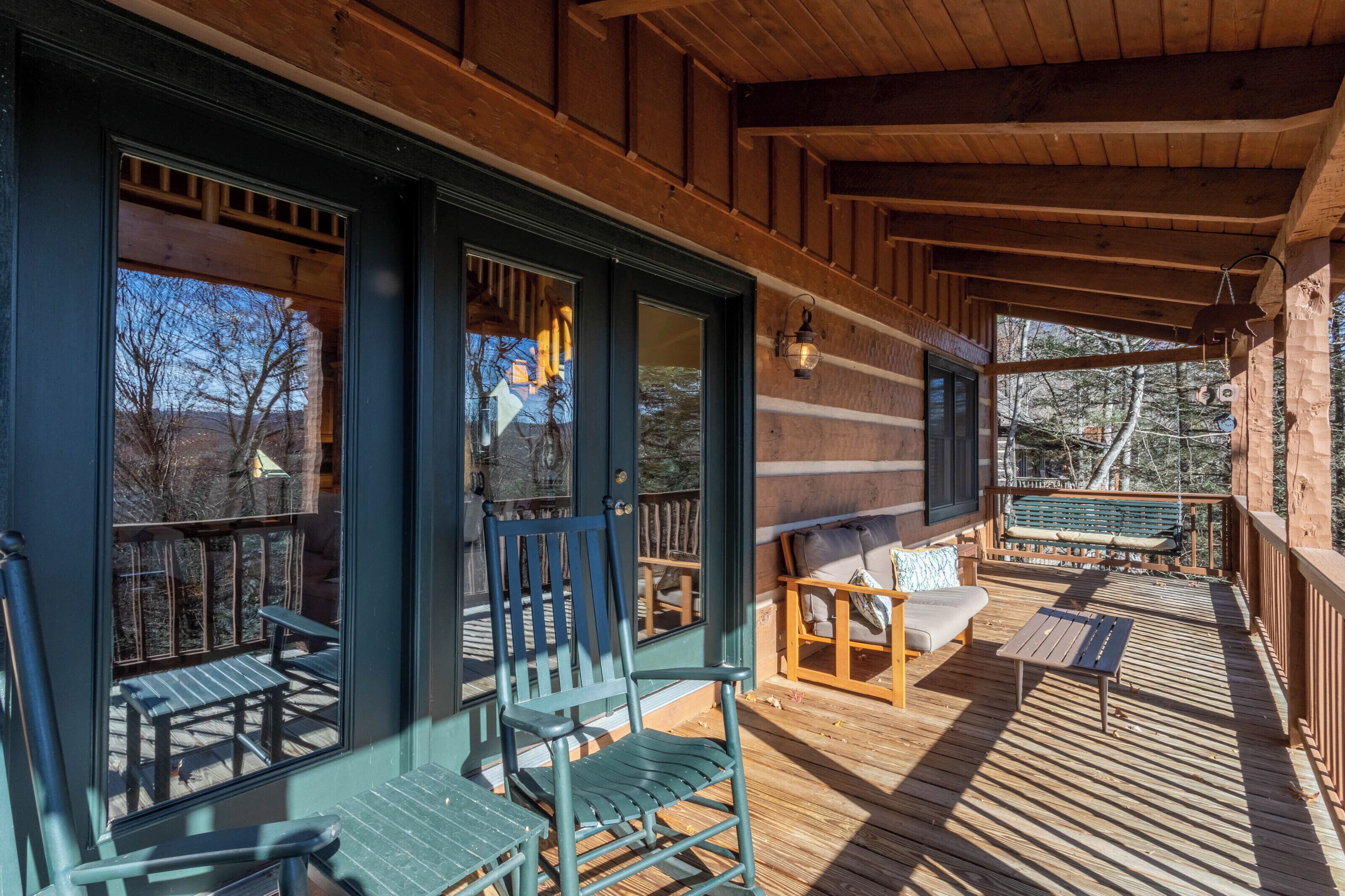 A wooden deck with outdoor seating, including chairs and a bench, and large windows offering views of the surrounding landscape.