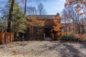 A wooden cabin with a covered porch, surrounded by trees and a gravel driveway. - Mountain Dream (Banner Elk)