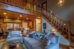 A spacious living room with a high ceiling, wooden staircase, and a cozy fireplace. - Mountain Dream (Banner Elk)