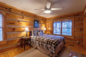 A cozy log cabin bedroom with a bed, two bedside tables, a ceiling fan, and a large window. - Mountain Dream (Banner Elk)