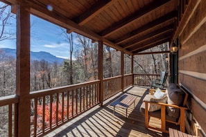 A wooden deck with a bench and chairs, overlooking a forested mountain range. - Mountain Dream (Banner Elk)