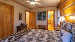 A bedroom with a bed, wooden wardrobe, a ceiling fan, a small table, and a wall with framed pictures. - Mountain Dream (Banner Elk)