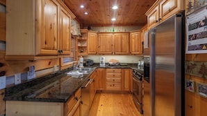 A kitchen with wooden cabinets, granite countertops, stainless steel appliances, and a wooden floor. - Mountain Dream (Banner Elk)