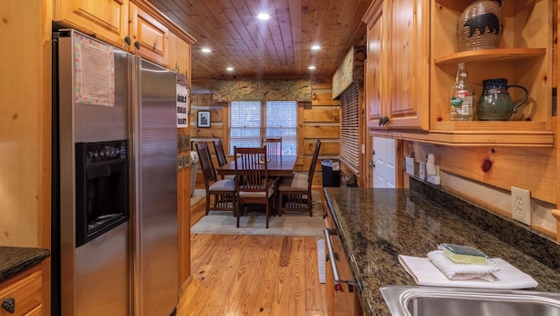 A wooden cabin kitchen with a refrigerator, dining table, chairs, and a granite countertop. - Mountain Dream (Banner Elk)
