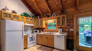 A kitchen with wooden cabinets, a refrigerator, stove, microwave, sink, and a view of the outdoors. - Trillium (Banner Elk)