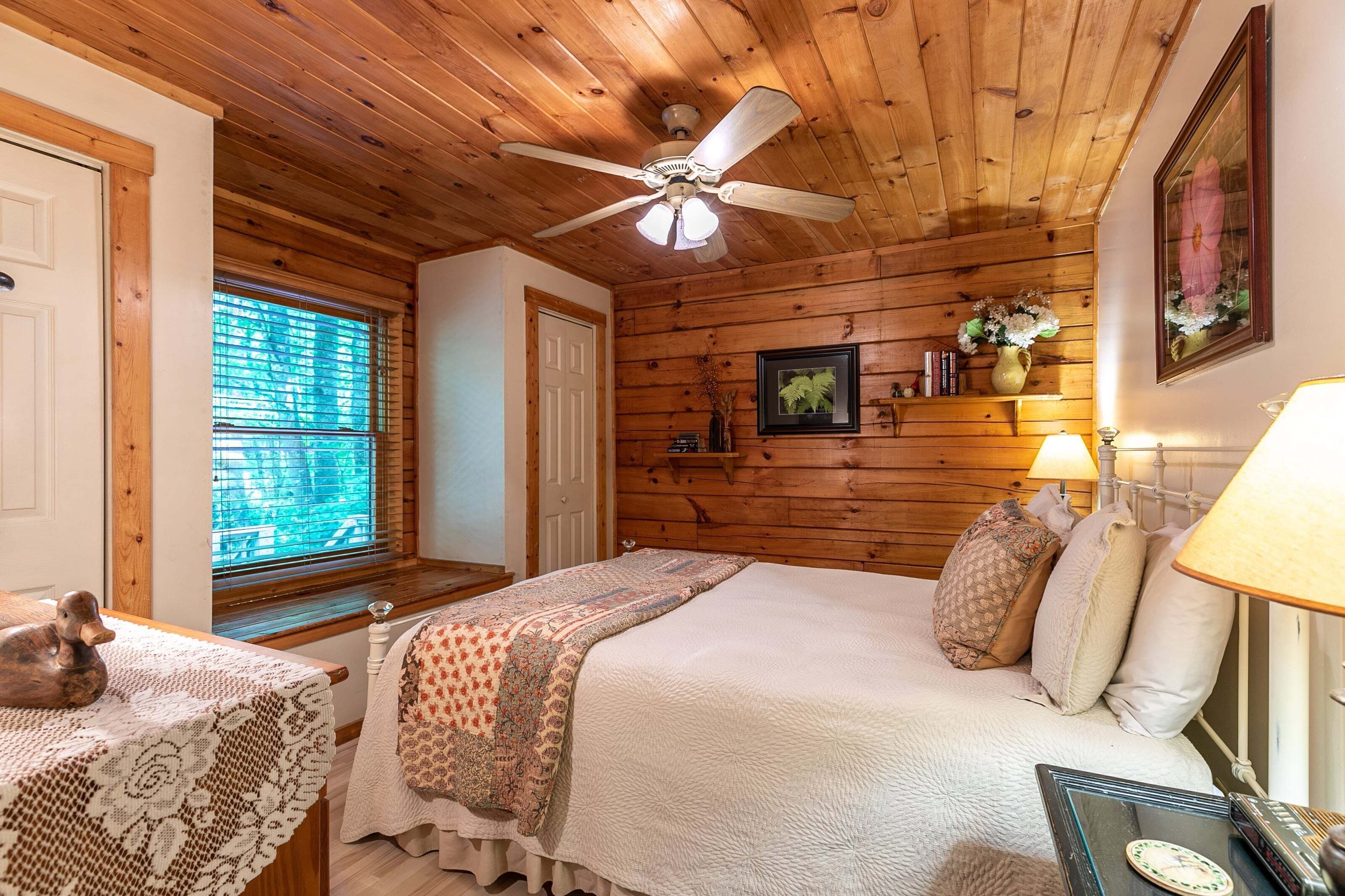 A wooden-paneled bedroom with a bed, a nightstand, a lamp, and a ceiling fan.