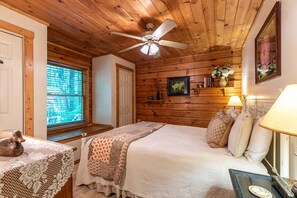 Ein Schlafzimmer mit Holzwandverkleidung, einem Bett, einem Nachttisch, einer Lampe und einem Deckenventilator.