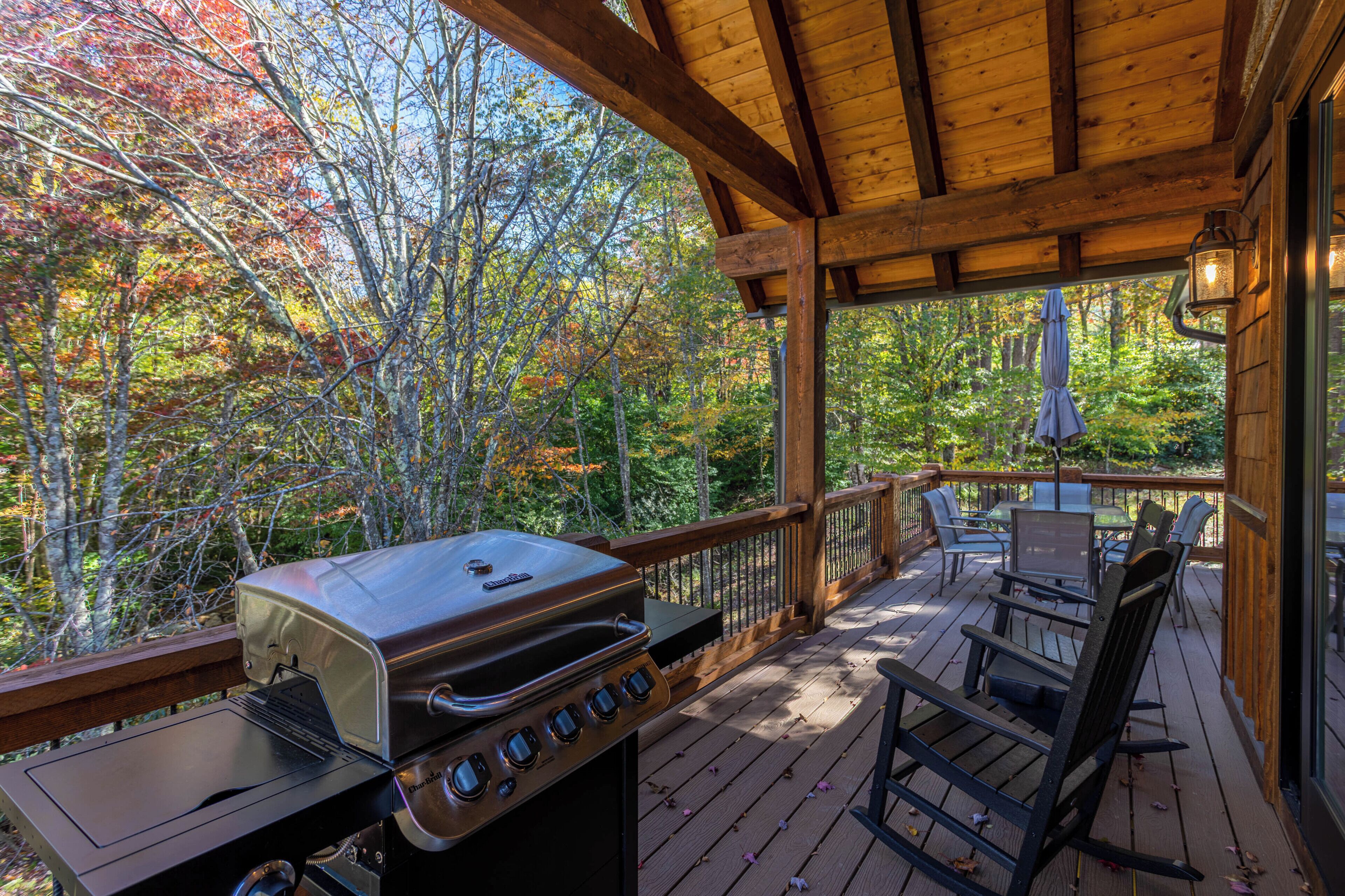A covered outdoor deck with a grill, chairs, and a table.