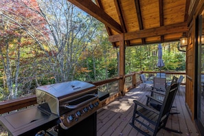 Eine überdachte Terrasse im Freien mit Grill, Stühlen und Tisch.