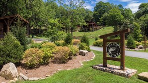 A lodge entrance with a sign, surrounded by lush greenery and a stone pathway. - Red Wolf Chalet at Eagles Nest (Banner Elk)