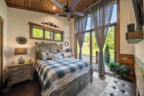 Ein Schlafzimmer mit einem Bett, Nachttischen, einem Deckenventilator, einem Fenster mit Vorhängen und Blick ins Freie.