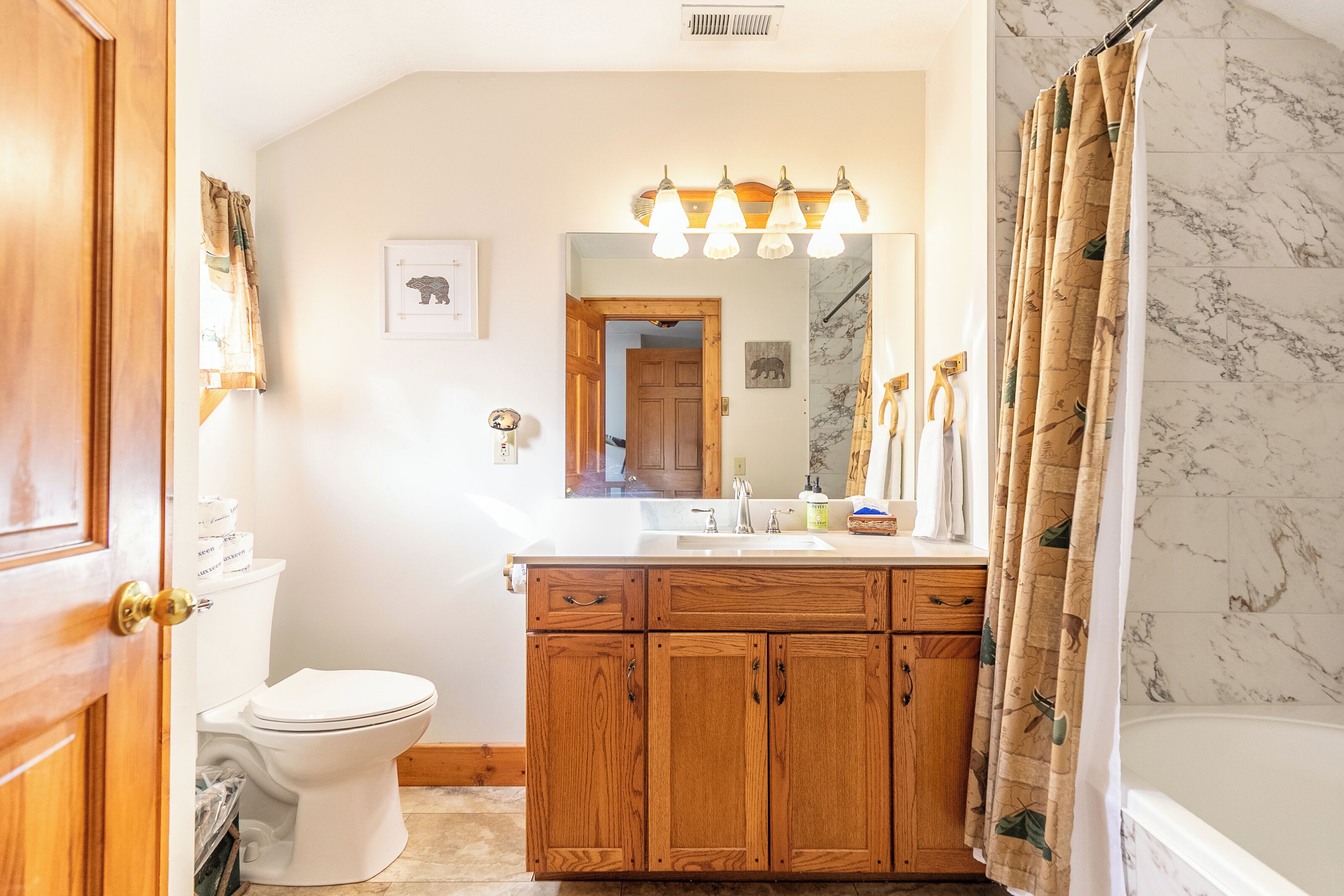 A bathroom with a wooden vanity, a white toilet, a mirror with lights, and a shower curtain.