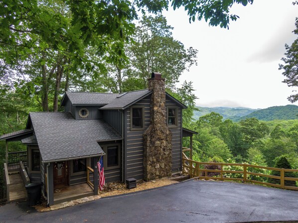 A cabin with a stone chimney, a porch, and a view of the surrounding forest.