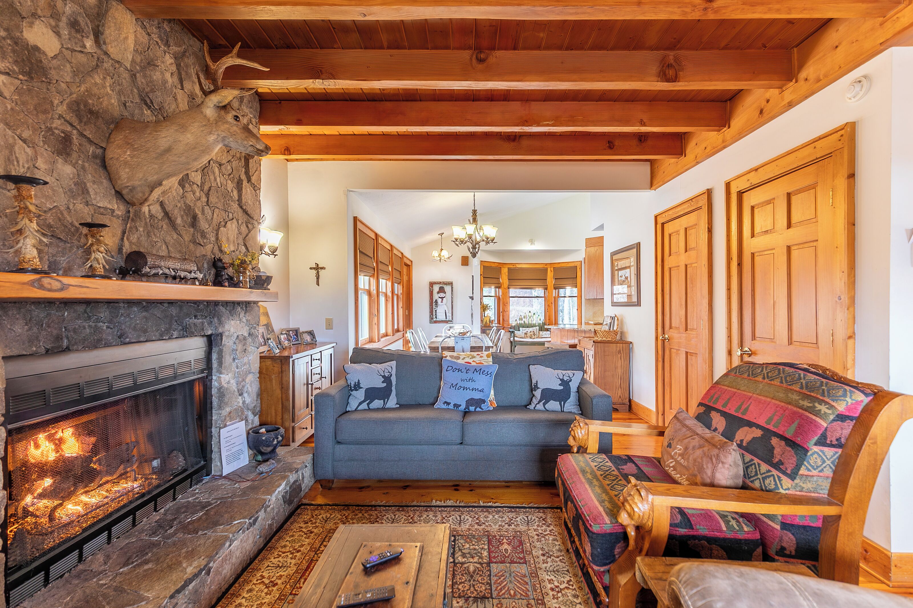 A cozy living room with a stone fireplace, a sofa with deer-themed pillows, and a colorful woven ottoman.