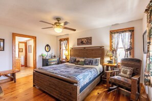 A wooden bed with a headboard, a ceiling fan, a wooden chair, a bedside table, and a window with curtains.