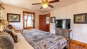 A bedroom with a bed, a ceiling fan, a television on a wooden stand, and two framed pictures on the wall.