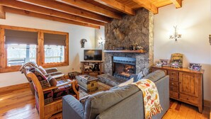 A cozy living room with a stone fireplace, wooden beams, a television, and a sofa.