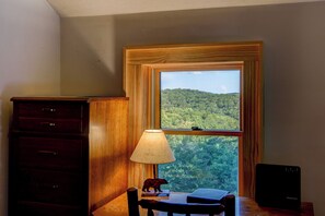 Une pièce avec un bureau, une lampe, une figurine d’ours et une vue sur une forêt, visible par la fenêtre.