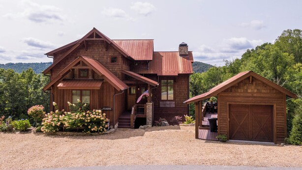 A rustic log cabin with a large porch, a separate garage, and a gravel driveway. - Birds Nest Retreat at Eagles Nest (Banner Elk)