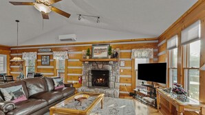 A log cabin interior with a fireplace, leather sofa, television, and wooden walls. - Sugars Sunset Vista (Banner Elk)