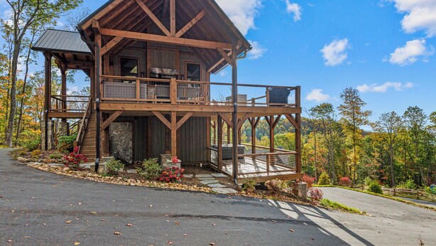 A two-story wooden cabin with a balcony, stone foundation, and a stone fireplace. - The Dire Wolf at Eagles Nest (Elk Park)