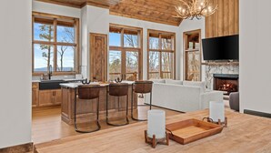 A modern kitchen with a stone fireplace, wooden bar stools, and a large TV. - The Dire Wolf at Eagles Nest (Elk Park)