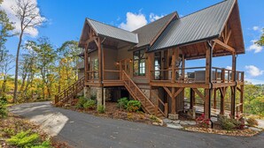 A wooden cabin with a stone foundation, a covered porch, and a staircase leading to the upper level. - The Dire Wolf at Eagles Nest (Elk Park)