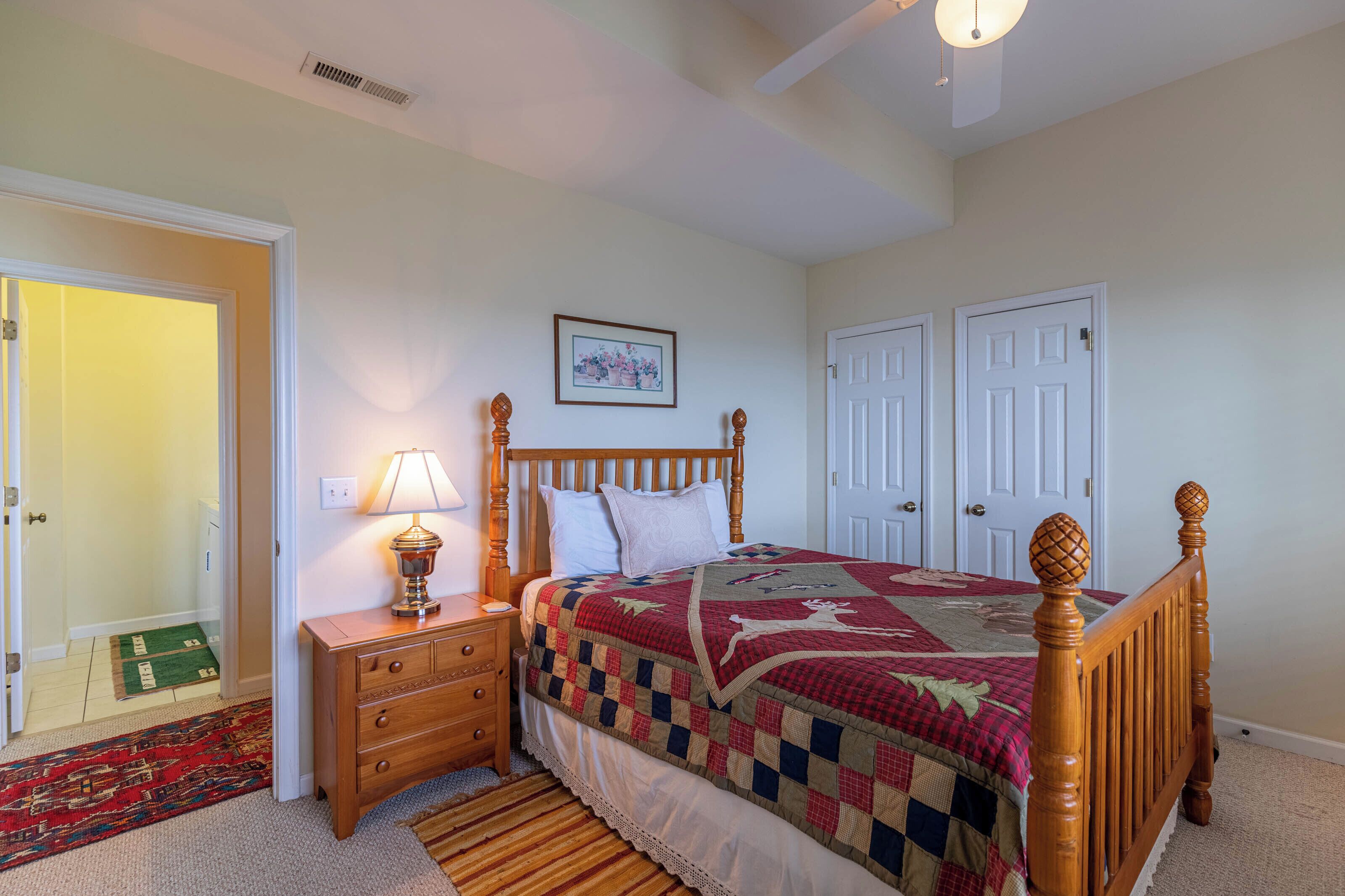 A bedroom with a wooden bed, a nightstand with a lamp, a quilt, and two doors.
