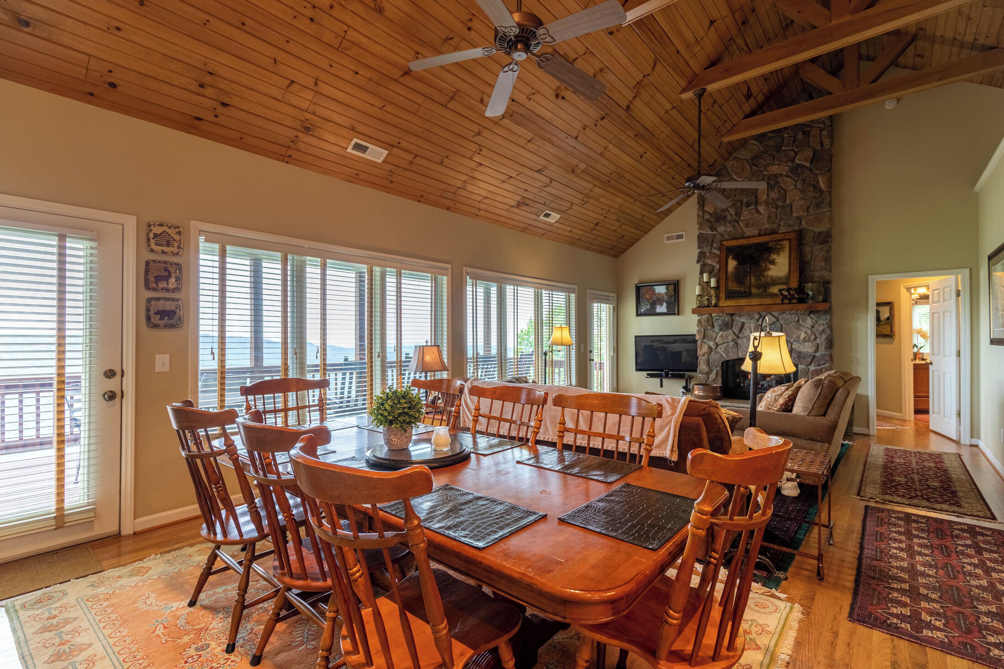 A spacious dining area with a large wooden table and chairs, a stone fireplace, and a cozy seating area with a couch and a television.