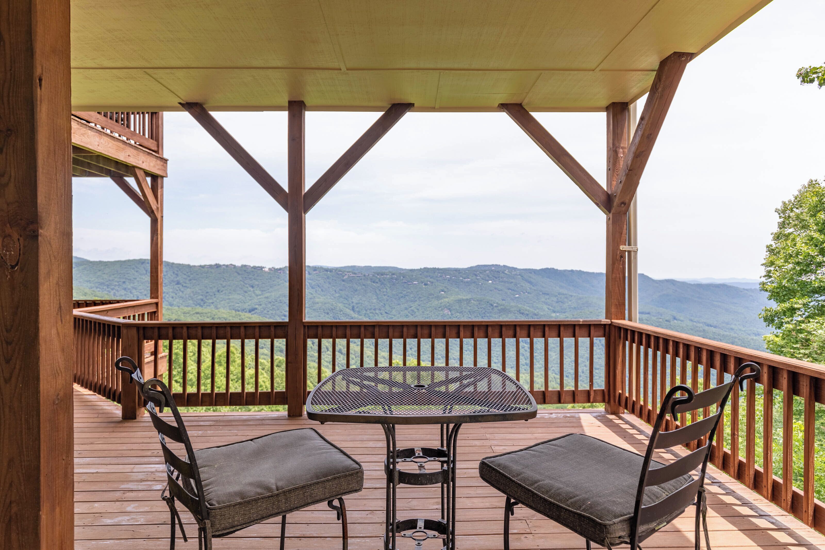 A wooden deck with a table and two chairs, overlooking a mountainous landscape.