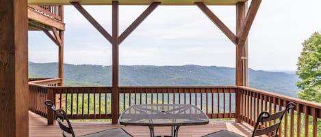 A wooden deck with a table and two chairs, overlooking a mountainous landscape.
