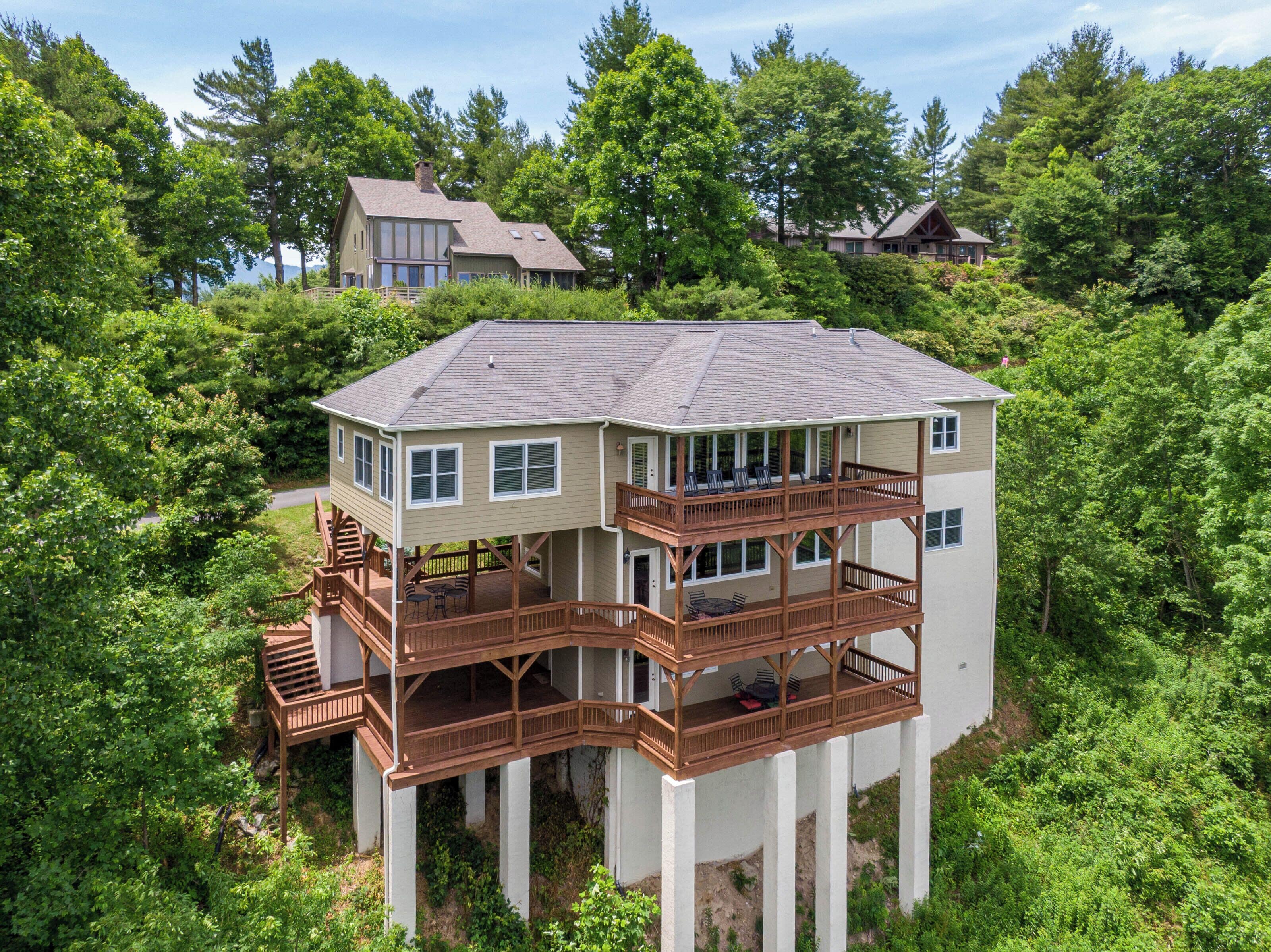 A multi-story house with a deck, surrounded by dense greenery.