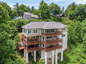 A multi-story house with a deck, surrounded by dense greenery. - Hangin' Out - Stunning Mountain Views, Garage, Jacuzzi Tub (Blowing Rock)