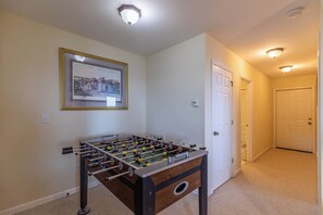 Ein Zimmer mit einem Kicker, einem gerahmten Bild an der Wand und einer Tür zu einem anderen Raum.