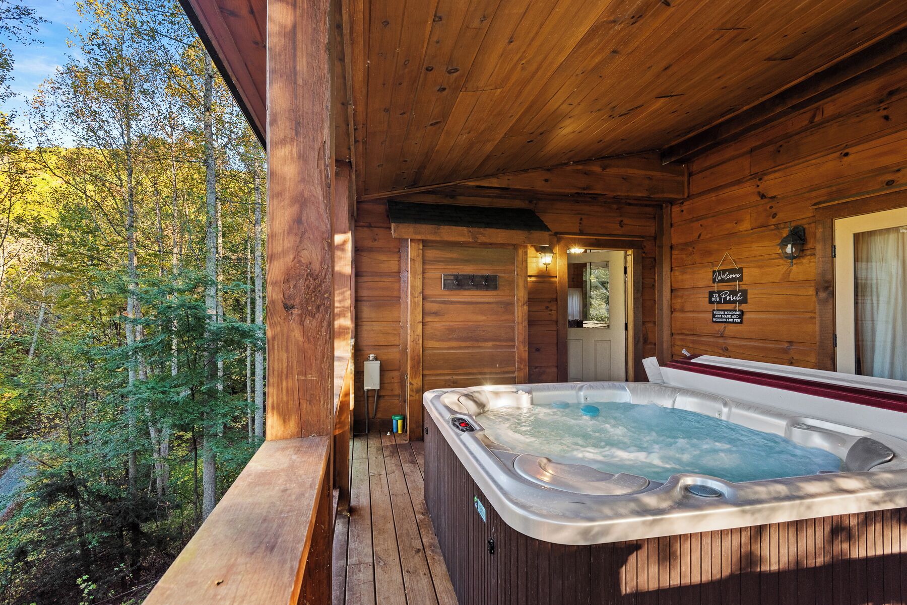 A wooden cabin with a hot tub on a deck, surrounded by trees.