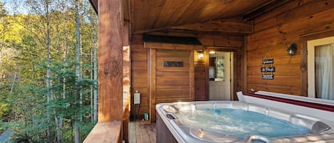Een houten blokhut met een jacuzzi op een terras, omringd door bomen.