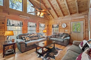 Ein gemütliches Blockhaus-Interieur mit zwei Sofas, einem Couchtisch und einem Deckenventilator.