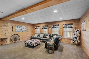 A log cabin interior with a leather sofa, a wooden rocking chair, a small table, and a decorative wheel. - Falling Waters (Banner Elk)