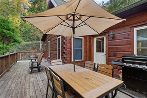 A wooden deck with a table and chairs, a barbecue grill, and a large umbrella. - Falling Waters (Banner Elk)