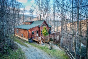 Eine Holzblockhütte mit einer Veranda und einer kleinen Terrasse, umgeben von Bäumen.