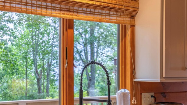 Eine Küche mit einer Granitabdeckung, einer Spüle, einem Wasserhahn, einem Fenster mit Blick auf Bäume und Holzbalken an der Decke.