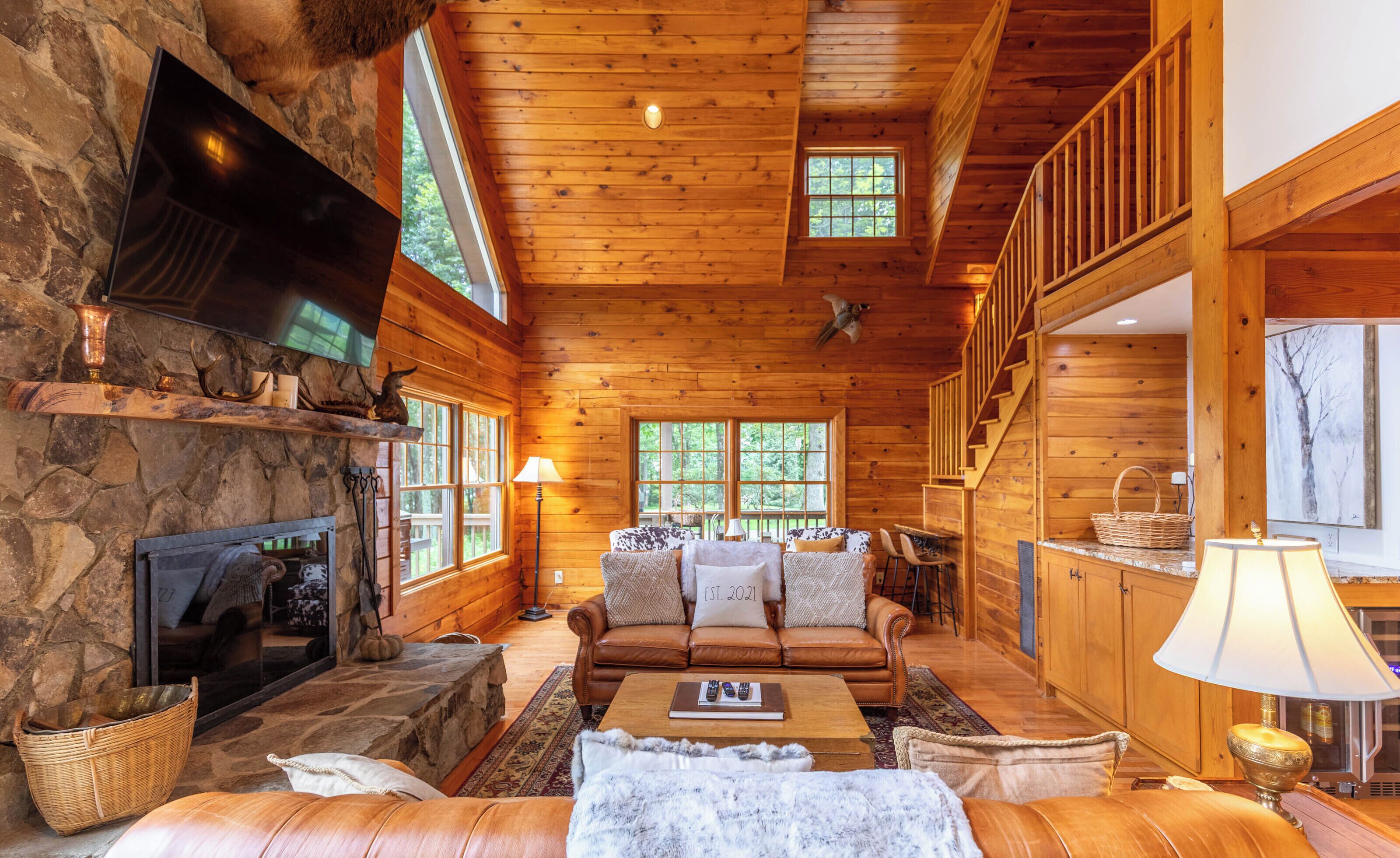 A log cabin interior with a stone fireplace, wooden walls, a sofa set, and a dining area.