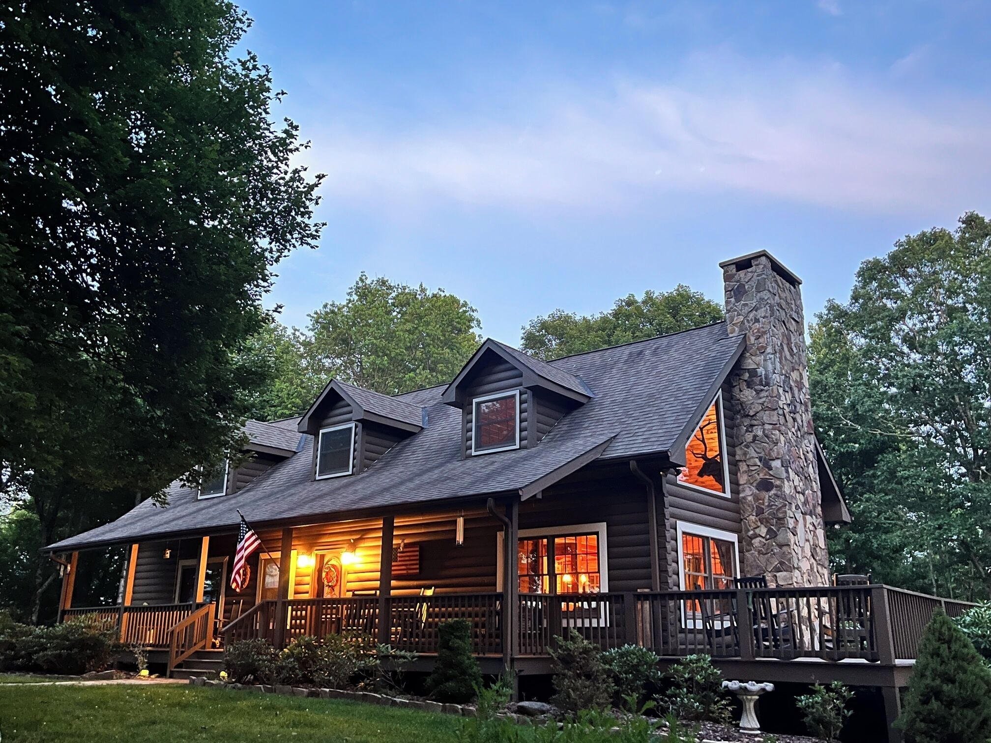A log cabin with a stone chimney, multiple windows, and a porch.