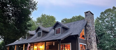 A log cabin with a stone chimney, multiple windows, and a porch.