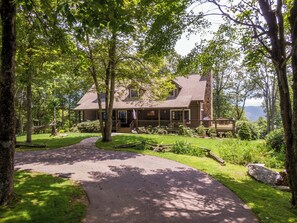 A cabin with a porch, surrounded by trees and a paved path leading to the entrance. - Mountaintop at Yonahlossee Saddle Club (Boone)