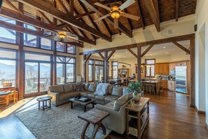 A spacious living room with a large sectional sofa, wooden beams, and large windows offering mountain views. - Banner Crest - Mountain Luxury! Views, hot Tub, Private Pool and Tennis Courts, Game Room (Banner Elk)